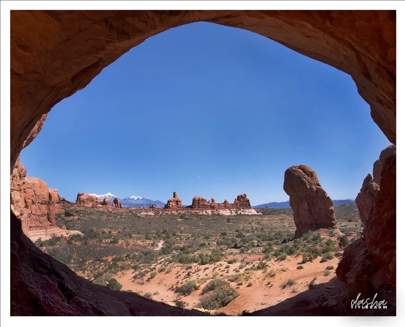 Taos Rock Arch Vista, Red rock desert of Taos framed through a natural arch with distant mountains beyond.